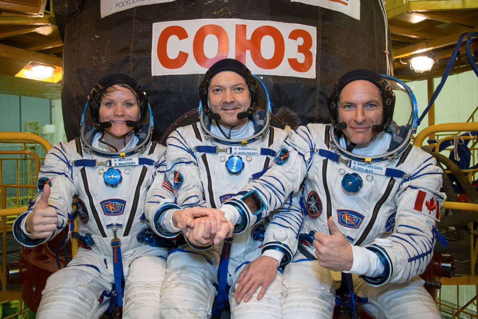 In the Integration Facility at the Baikonur Cosmodrome in Kazakhstan, Expedition 58 crew members Anne McClain of NASA (left), Oleg Kononenko of Roscosmos (center) and David Saint-Jacques of the Canadian Space Agency (right) pose for pictures Nov. 20 in front of their Soyuz MS-11 spacecraft.<br />Credits: NASA/Victor Zelentsov